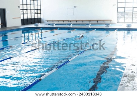 A lone swimmer practices in an indoor pool, with copy space. The setting suggests a focus on fitness or training, in a school or community center. Royalty-Free Stock Photo #2430118343