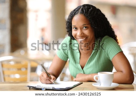 Happy black woman filling form in a bar terrace looking at you
