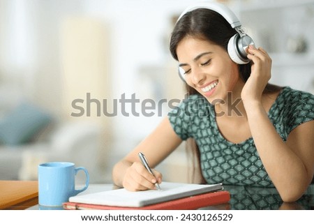 Happy student with headphone studying listening audio guide and taking notes at home