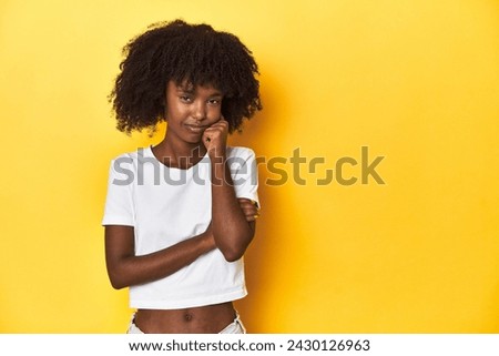 Teen girl in classic white T-shirt, yellow studio backdrop who feels sad and pensive, looking at copy space.
