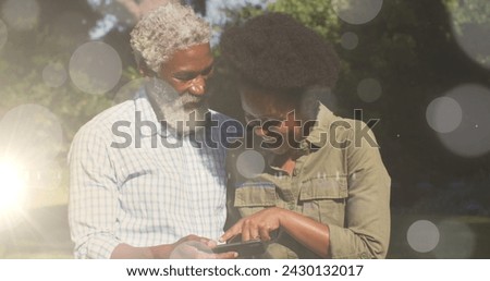 Image of light spots over african american couple using smartphone. Valentine's day, love and celebration concept digitally generated image.