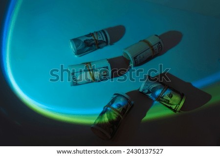 Tubes of hundred dollar bills rewound with a rubber band under blue light. High quality photo
