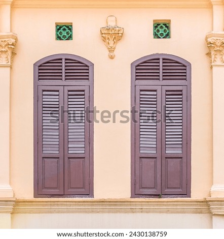 Elegant Colonial Windows with Decorative Lamp, Twin colonial windows with shutters paired with a decorative wall lamp and ornate details on a peach-colored facade.
