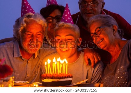 Grandfathers senior people and young teenager celebrate birthday together by night at home with cake and candles having fun and enjoying love and friendship at the party with different generations