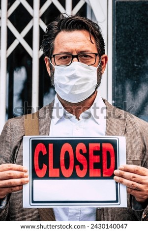 Adult professional businessman with closed sign outside his store for coronavirus economy crisis emergency for lockdown at home - business recession concept with owner outdoor shop