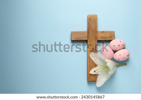 Wooden cross, painted Easter eggs and lily flower on light blue background, top view. Space for text
