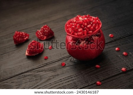 A ripe, red pomegranate is beautifully cut, posing on a wooden black table. Healthy, wholesome, dietary food.