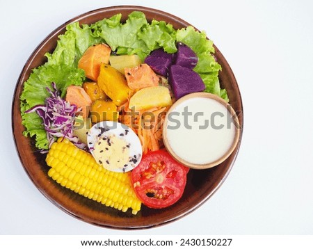 Fruit and vegetable salad with salad dressing in a wooden bowl placed in a plate on a white background with pumpkin, corn, sweet potato, carrot, lettuce, cabbage, tomato, boiled egg and poppy.