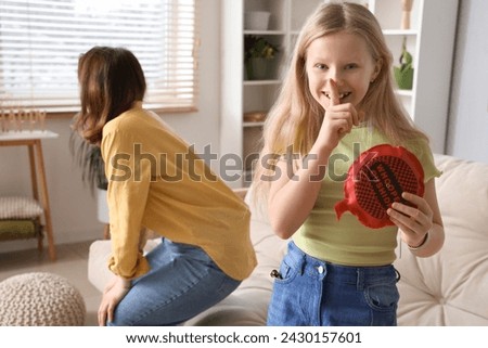 Funny little girl with whoopee cushion showing silence gesture and her mother at home. April Fools' Day celebration Royalty-Free Stock Photo #2430157601