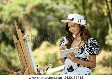 Smiling young woman in casual dressed painting on canvas in the park. Art and leisure activity concept