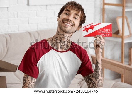 Young tattooed man with gift voucher at home