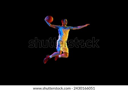 Powerful Sam Dunk. Athletic man, basketball player in mid air jumping to make goal against black studio background in mixed neon light. Concept of professional sport, energy, match, championship.