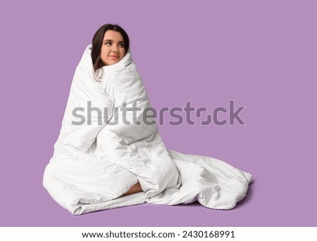 Beautiful young happy woman wrapped in blanket sitting on purple background