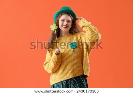 Young woman in Leprechaun's hat with paper clover on orange background. St. Patrick's Day celebration