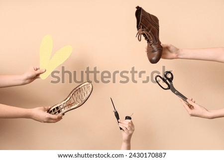 Female hands with shoe pieces, craft tools and insoles on beige background. Shoes repair concept