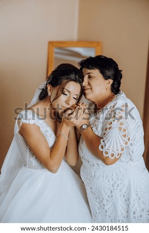 A beautiful and happy mother and her daughter, the bride, are standing next to each other. The best day for parents. Tender moments at the wedding. Royalty-Free Stock Photo #2430184515