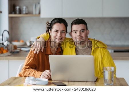 Mom teaching young man with down syndrome, using laptop. Telehealth consultation with doctor. Royalty-Free Stock Photo #2430186023