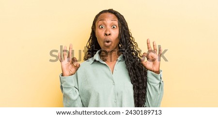 black pretty woman feeling shocked, amazed and surprised, showing approval making okay sign with both hands