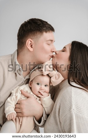 Man kisses woman. Father, mother hugging daughter. Happy family hugs cute baby on a holiday closeup. Dad, mom holds in hands 6 month old little kid. Daddy, mommy embracing girl isolated on white wall.