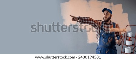 Painter man holding a paint roller surprised and pointing finger on advertising place. Banner. Copy space