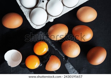 Brown and white chicken eggs next to broken eggs on a dark background