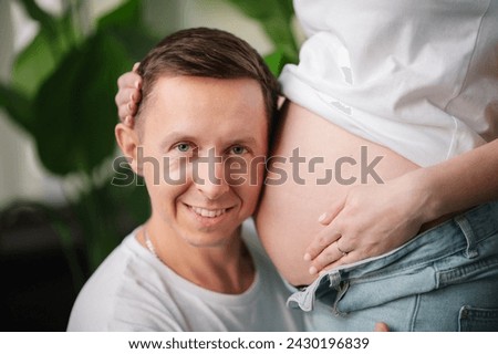 Cropped image of husband listens baby in belly pregnant wife. Pregnant woman and loving handsome man hugging tummy at home. Parenthood concept. Couple waiting baby. Nine months closeup.