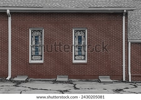 The red brick wall of a small community church is adorned with humble stained glass windows.