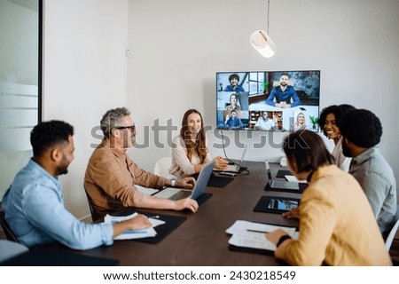 A lively and productive team meeting is captured where colleagues are connected via a large screen, showcasing a blend of in-person and remote collaboration. Virtual meeting concept Royalty-Free Stock Photo #2430218549