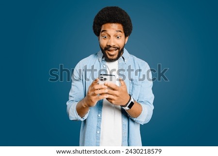 Young man looks surprised and excited using a smartphone, embodying a spontaneous moment of receiving unexpectedly good news, perfect for representing instant communication and its impact on emotions Royalty-Free Stock Photo #2430218579