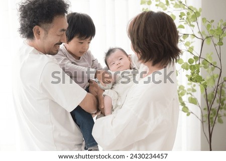 A Japanese couple holding their small children by a bright sunlit window in their living room.