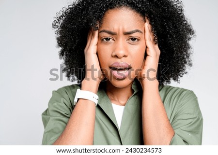 An African-American woman expresses stress or concern, hands pressed to her temples, her facial expression portraying a moment of anxiety or intense thought against a stark background Royalty-Free Stock Photo #2430234573