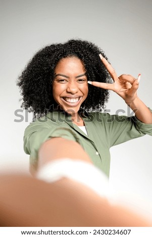 Engaging directly with the camera, an African-American woman makes a peace sign with her fingers, her smile and lively eyes conveying a playful yet professional persona in the digital era