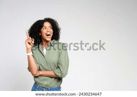 Radiating joy, an African-American woman points upwards, her face alight with excitement, indicating a new idea or a joyful exclamation on a plain backdrop Royalty-Free Stock Photo #2430234647