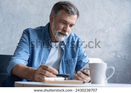 Smiling mature old man enjoying shopping in internet store using mobile phone applications, satisfied with fast money transfer secure service, entering payment information from credit card. Royalty-Free Stock Photo #2430238707