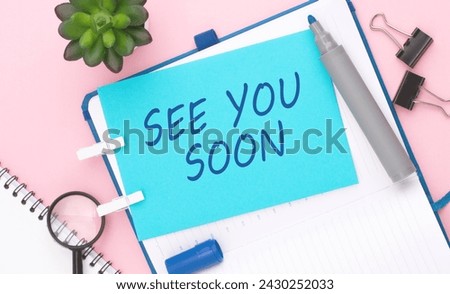 text 'SEE YOU SOON' on blue paper composition with stationery on color pink background. top view