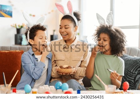 Portrait happy latin family eating chocolate eggs at home. Smiling mother and kids wearing bunny ears celebration Easter together. Holiday activity concept  Royalty-Free Stock Photo #2430256431