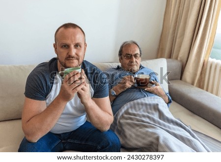 Cheerful grownup son and happy middle aged senior father enjoying coffee break in cozy living room at home, drinking tea, joking, laughing, talking, spending leisure time together, having fun.  Royalty-Free Stock Photo #2430278397