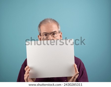 Sixty-year-old man holds up a blank white sign with room for copy on a blue background