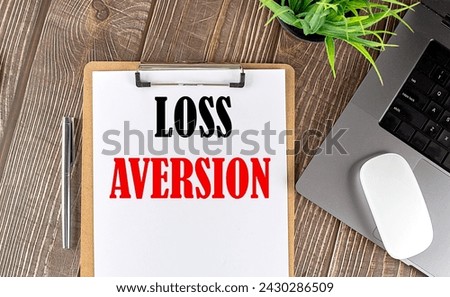LOSS AVERSION text on a paper clipboard with laptop and mouse on wooden background , business concept Royalty-Free Stock Photo #2430286509