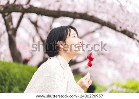 Japan tasty travel with sakura cherry blossom tree spring festival. Side view young adult asian woman eye closed. Eating japanese style street food strawberry candy.  Royalty-Free Stock Photo #2430290957