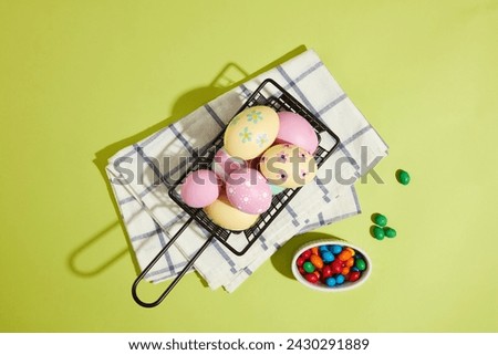 Concept of Easter Day with the composition of a basket containing a lot of colorful Easter eggs displayed on folded towel and a small bowl of candies. Easter means the celebration of hope