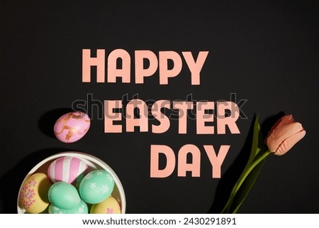 Top view of text “Happy Easter day" with tray of colorful eggs and flower decorated on black background. Scene for advertising