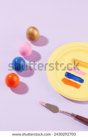 A vibrant collection of colorful Easter eggs arranged in a line, displayed with a yellow dish containing variety colors of paint. A palette knife decorated. Greetings and presents for Easter Day