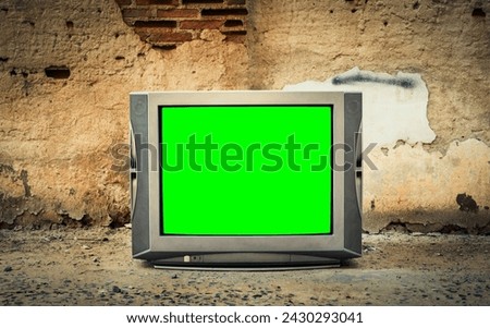 Vintage old TV on floor with green screen in front of old wall background.