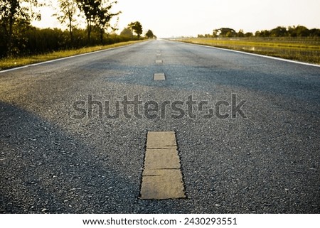 Close-up of asphalt road with yellow dividing line on rural road at evening in summer. Yellow center line dividing line on an empty road Royalty-Free Stock Photo #2430293551
