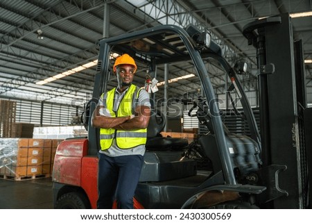 African forklift drivers focused on carefully transporting stock from shelves of a large warehouse wearing a helmet and vest looking toward goods