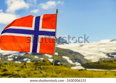 Norwegian flag waving against snowy mountains landscape, summertime. National tourist route Sognefjellet. Royalty-Free Stock Photo #2430306131