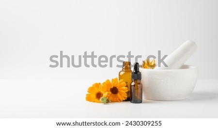 Calendula flowers in mortar and amber glass dropping bottles with essential oil. Marigold medicinal plant, herbal medicine, naturopathy and phytotherapy.