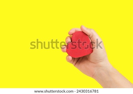 Heart in Hand Against Yellow Background. Evokes feelings of tenderness and sincerity, great for expressive visuals Royalty-Free Stock Photo #2430316781