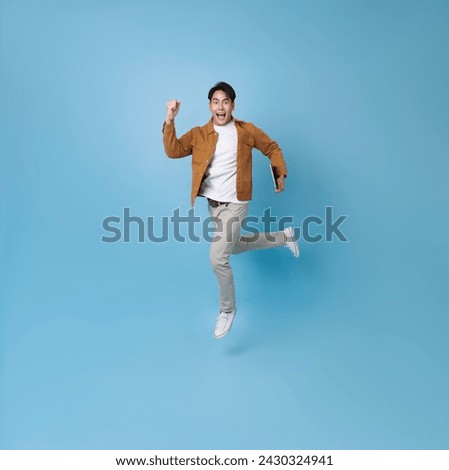 Full length Asian man holding tablet running with happy smile isolated on blue background. Happy man joyful run in copy space. 